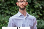 A man in a button down shirt and jeans standing outside with Sperling Interactive logo in the bottom left corner