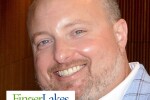 A man smiling wearing a blue sport coat with the Finger Lakes Community College Logo in the bottom left corner